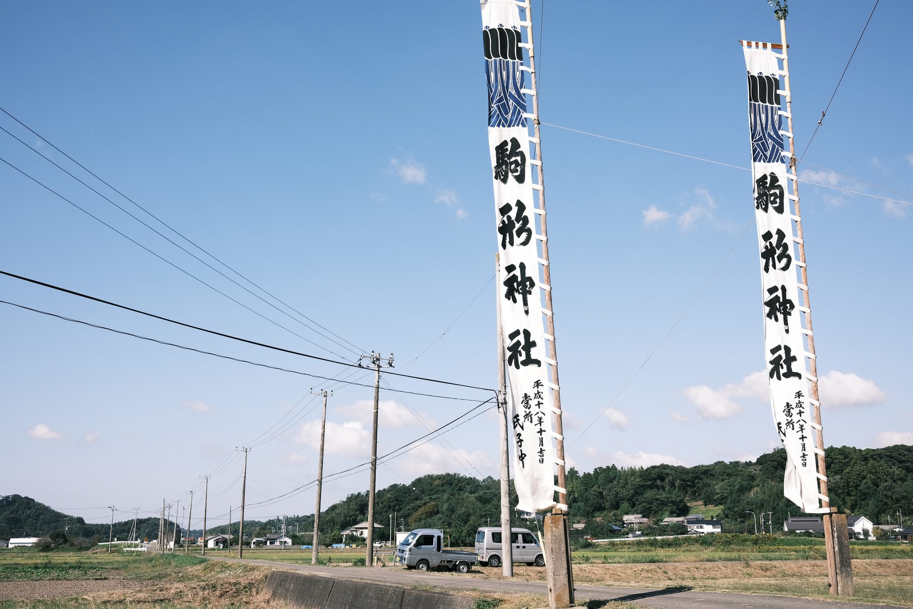 駒形神社の2本の幟旗が立つ農道。軽トラが停まり、奥に田園と里山が広がる南房総の日常風景